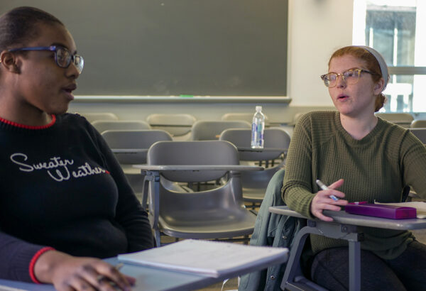 Two students stand with papers in their hands in discussion
