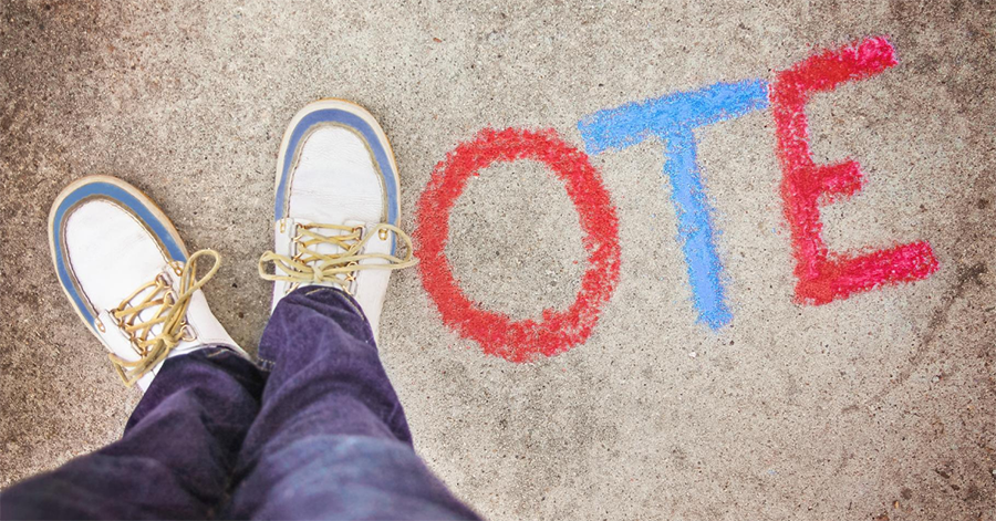 Vote written in sidewalk chalk with feet as the letter "V"