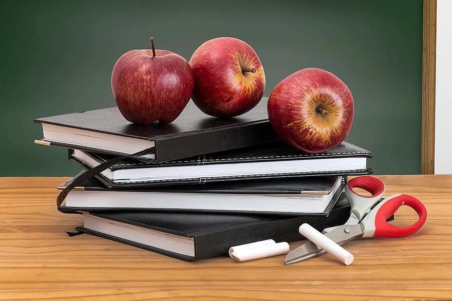 Red apples on stack of books with scissors and chalk