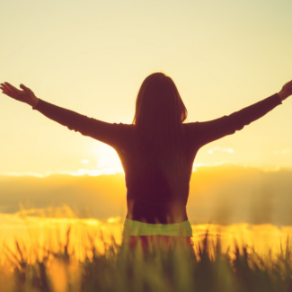 woman staring in field looking at sunset with arms outstretched
