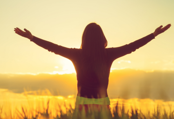 woman staring in field looking at sunset with arms outstretched
