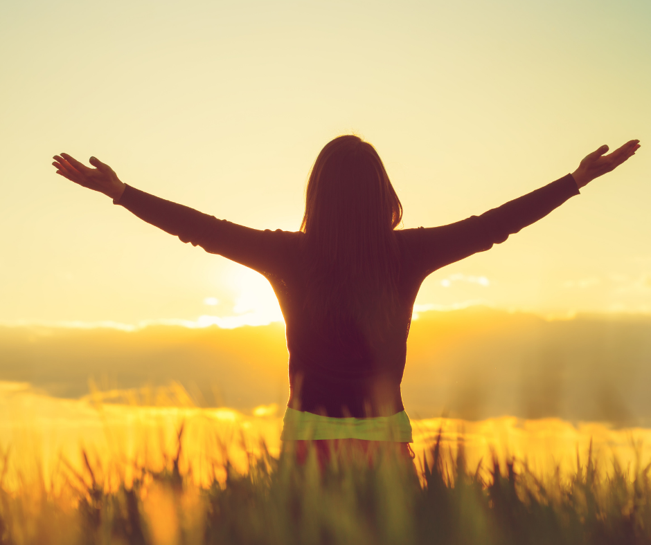 woman staring in field looking at sunset with arms outstretched