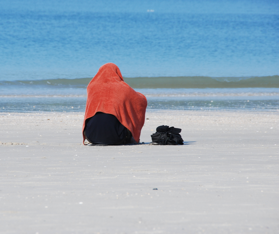 person sitting on beach wrapped in blankets
