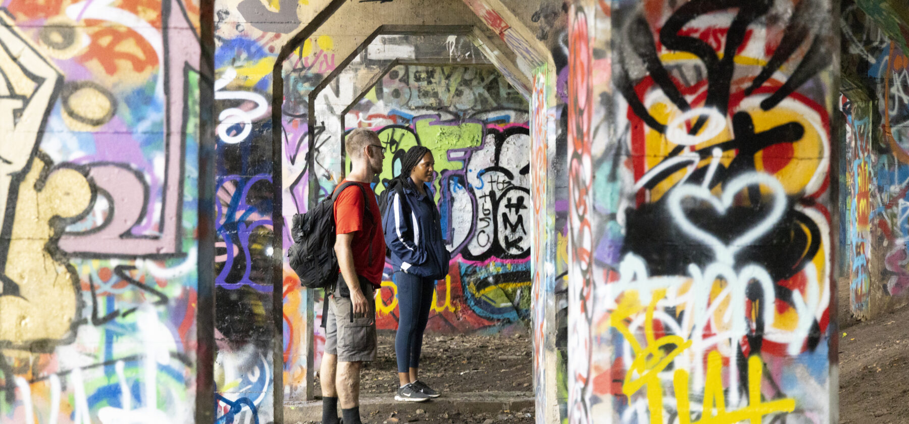 Two people stand among heavily graffitied underpass pillars in Philadelphia's Graffiti Pier