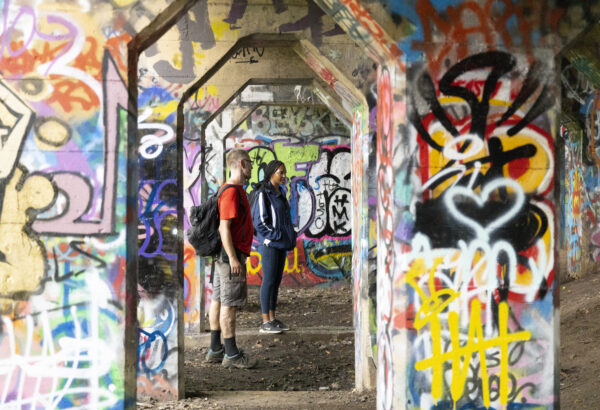 Two people stand among heavily graffitied underpass pillars in Philadelphia's Graffiti Pier