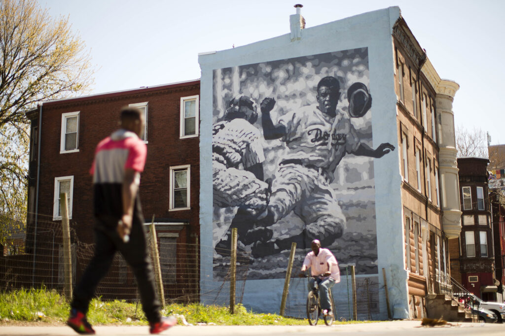 Person walking towards a mural of Jackie Robinson. There is someone bicycling towards the other person.