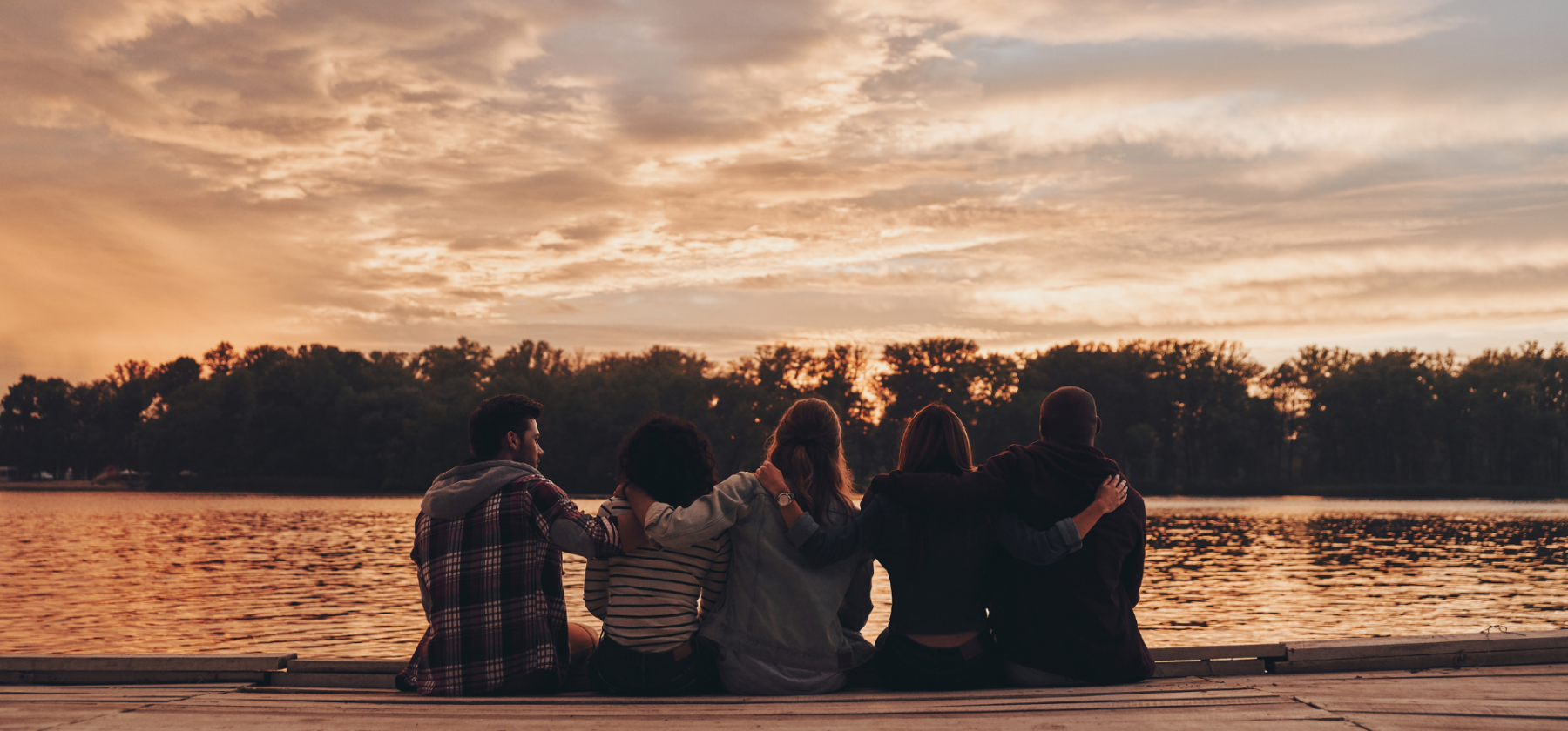 Friends sitting next to lake watching sunset
