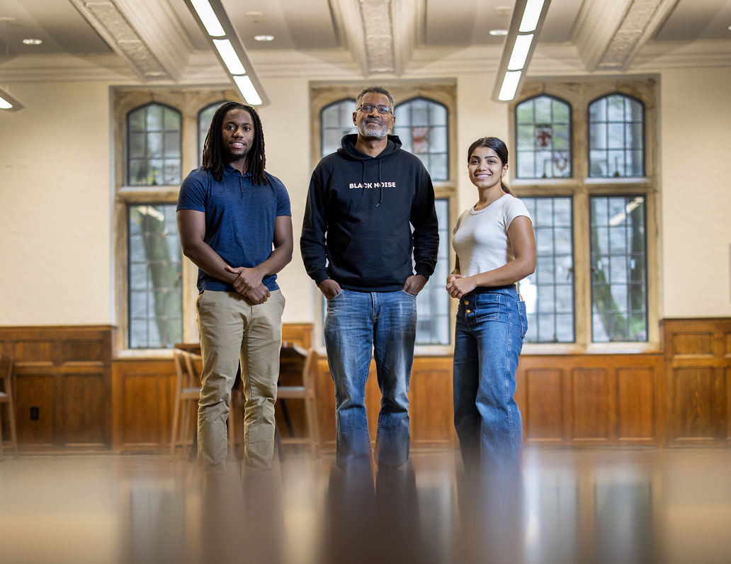 Three people, two students on either side of a professor smiling for the camera.