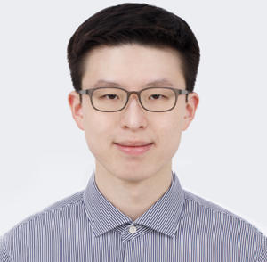 Headshot of man with short black hair and glasses smiling at camera against a white background wearing a light blue colored shirt