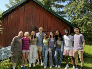 Group photo of 9 individuals ranging in age smiling in front of a red barn.