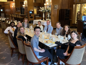 Group photo of people seated at table over a meal smiling at camera.