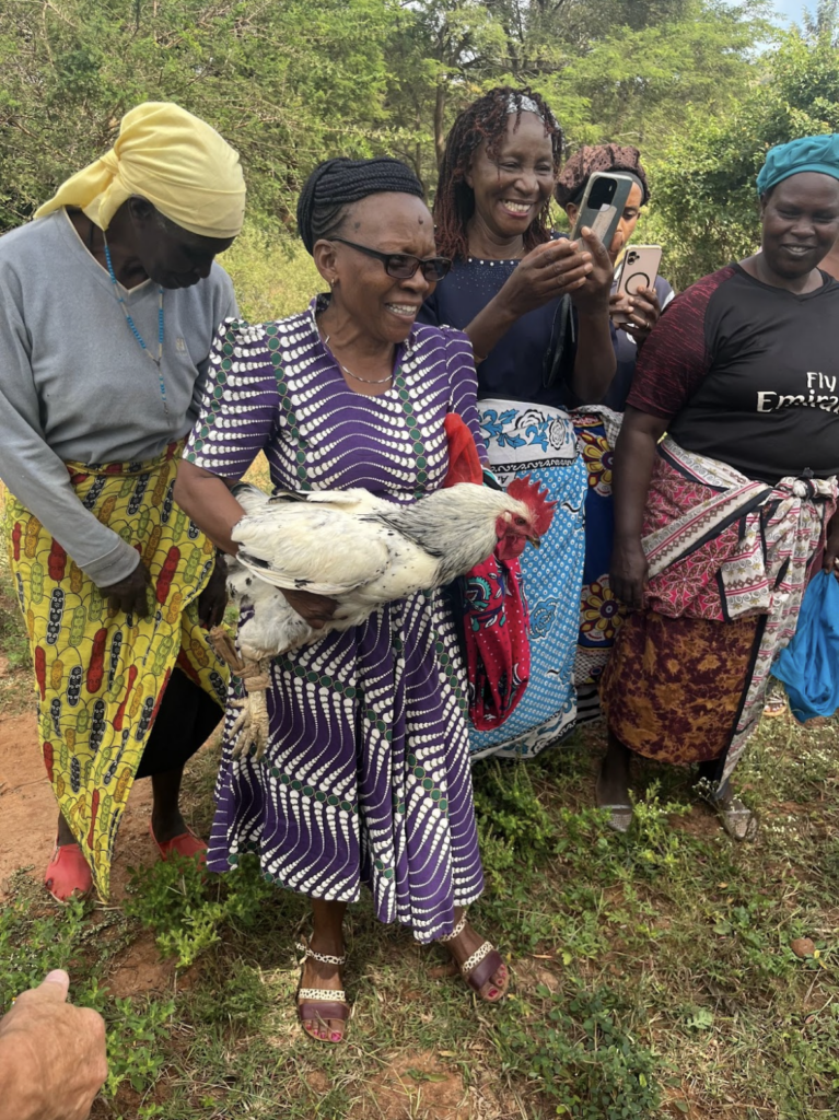 Women gathered smiling with one woman holding a rooster.