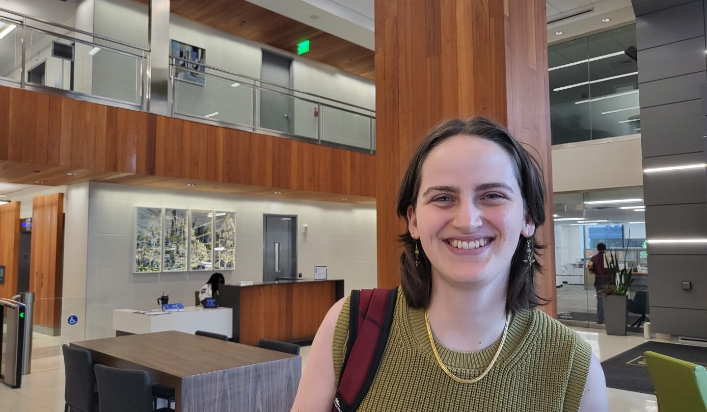 young woman with short brown hair smiling at the camera standing in lobby of office building