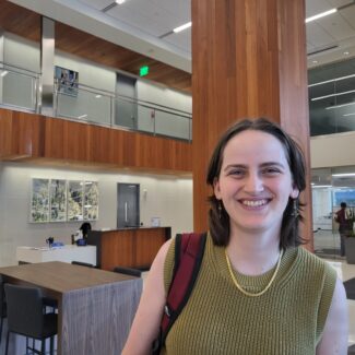 young woman with short brown hair smiling at the camera standing in lobby of office building