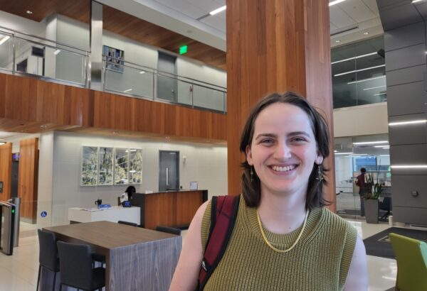 young woman with short brown hair smiling at the camera standing in lobby of office building