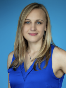 headshot for woman with light skin and shoulder length blonde hair smiling for camera wearing royal blue blouse against a blue background