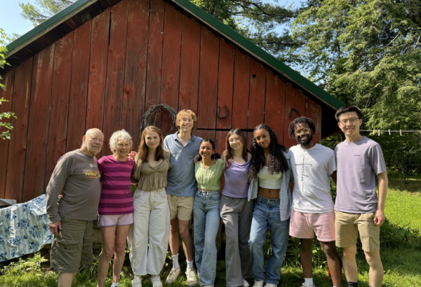 group photo of 9 people, in front of a red barn smiling and posed in a line for the camera