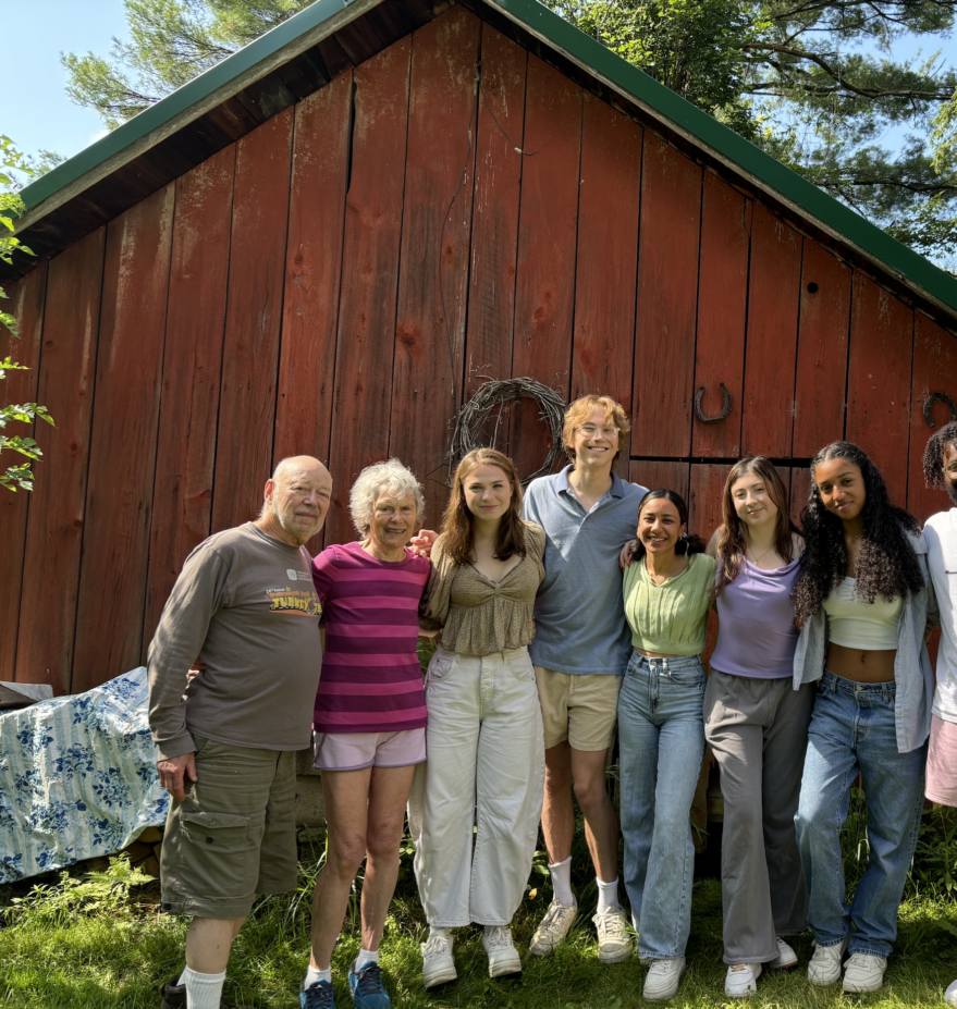 group photo of 9 people, in front of a red barn smiling and posed in a line for the camera