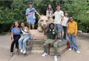 Students sitting around the statue of the Penn State Nittany Lion smiling for a picture.