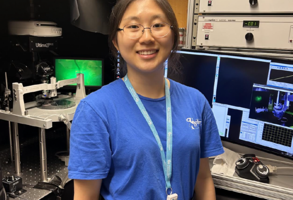 young woman smiling at camera in lab in front of computers and equipment.