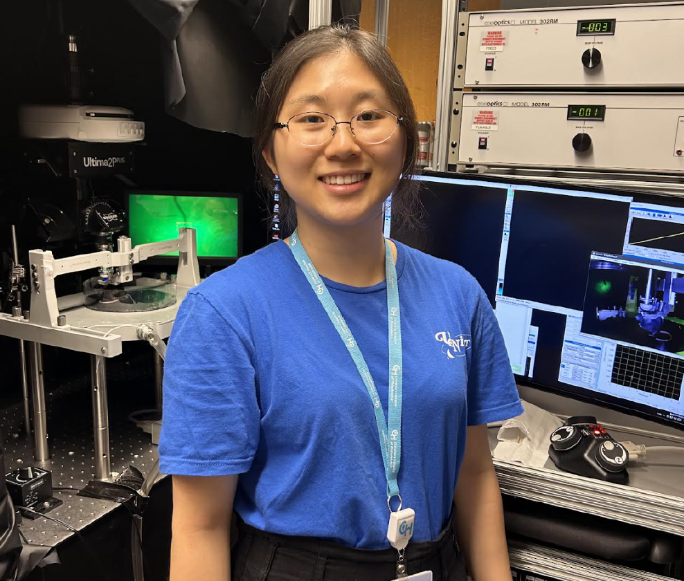 young woman smiling at camera in lab in front of computers and equipment.