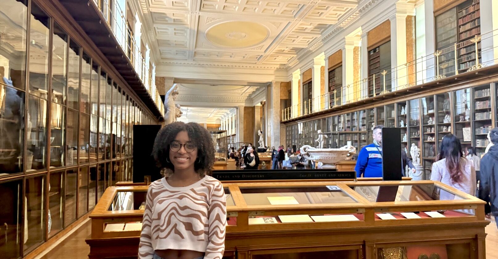 female student at the British Museum in London standing in front of display cases smiling for camera