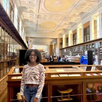 female student at the British Museum in London standing in front of display cases smiling for camera