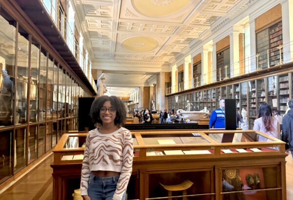 female student at the British Museum in London standing in front of display cases smiling for camera