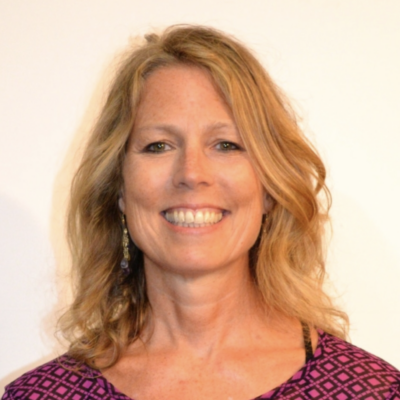 headshot for professor. woman with light skin, long blonde hair, wearing a pink and red patterned top