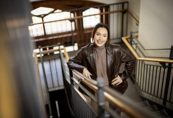 photo of program fellow on stairs smiling up at camera. she has light skin and brown hair pulled back and is wearing a brown leather jacket