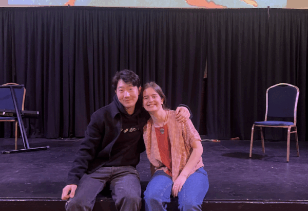 Two students seated on a stage smiling at the camera with a projection of a Matisse painting with dancers in a circle.