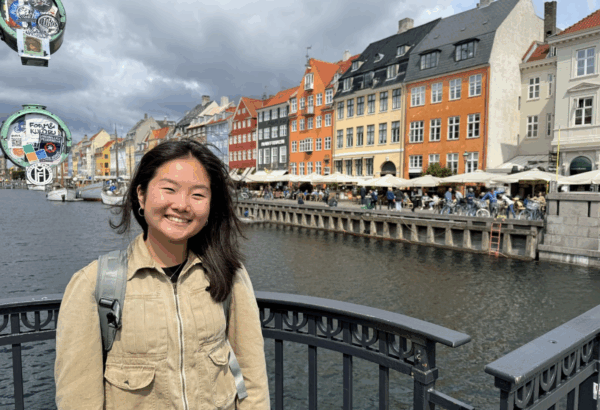 author in front of scenic background with water and buildings.