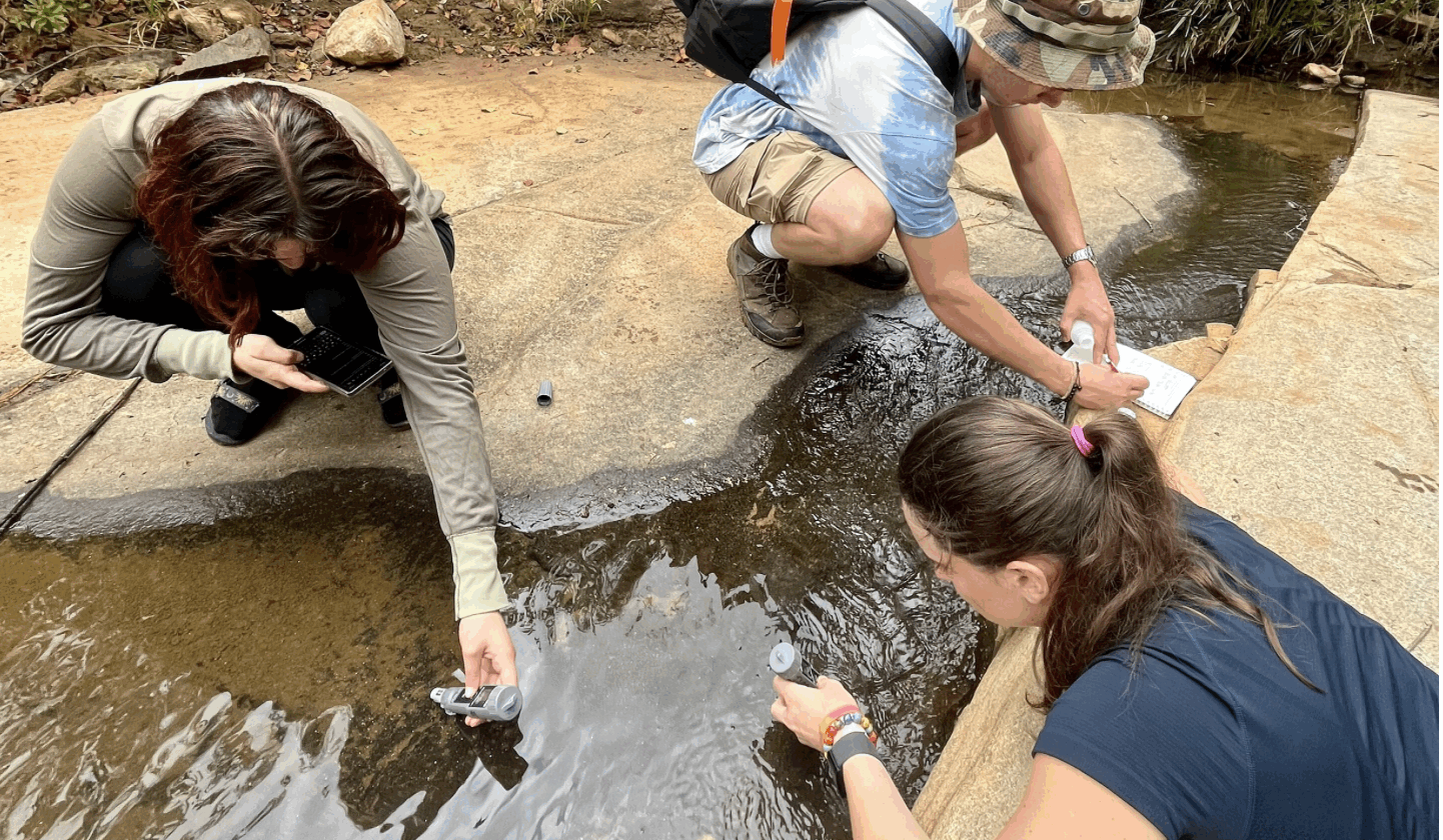 Photo of Griffin Pitt, with two other student researchers to test the conductivity, total dissolved solids, salinity, and temperature of water below a sand dam in Kenya.