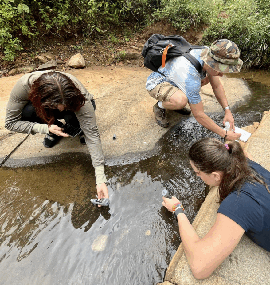 Photo of Griffin Pitt, with two other student researchers to test the conductivity, total dissolved solids, salinity, and temperature of water below a sand dam in Kenya.