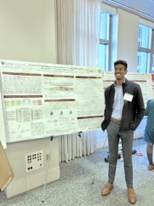 alumni Alex Eaton in front of his presentation poster at a conference